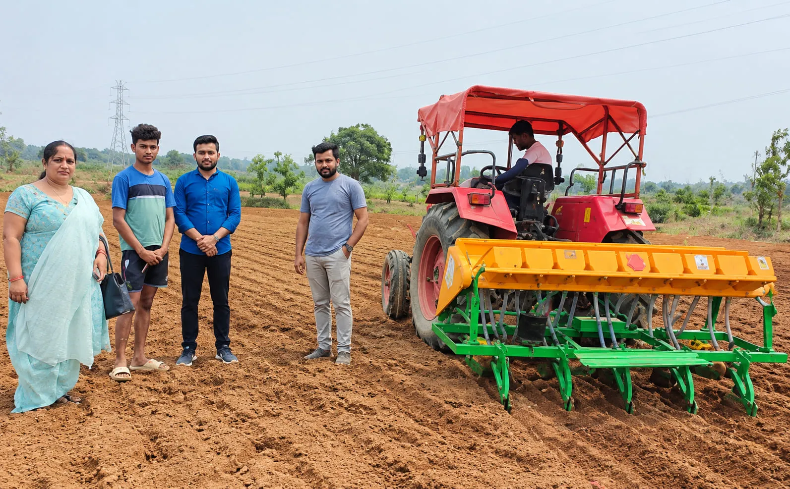 A tractor-drawn seed drill sowing paddy directly into a prepared field, watched by farmers