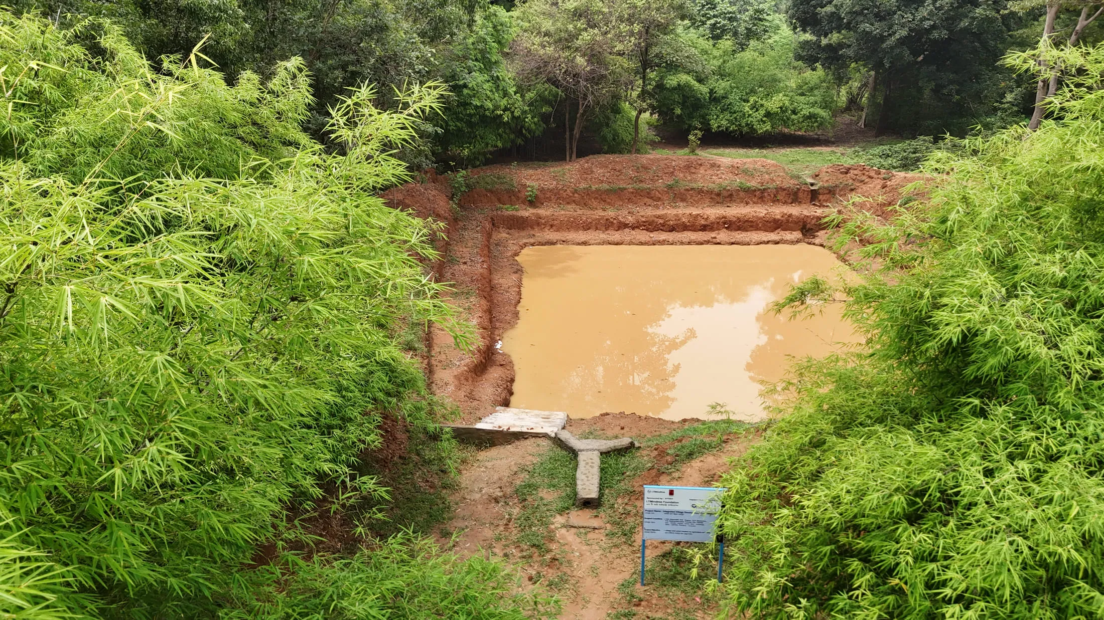 A completed farm pond holding water, with the project signboard beside it